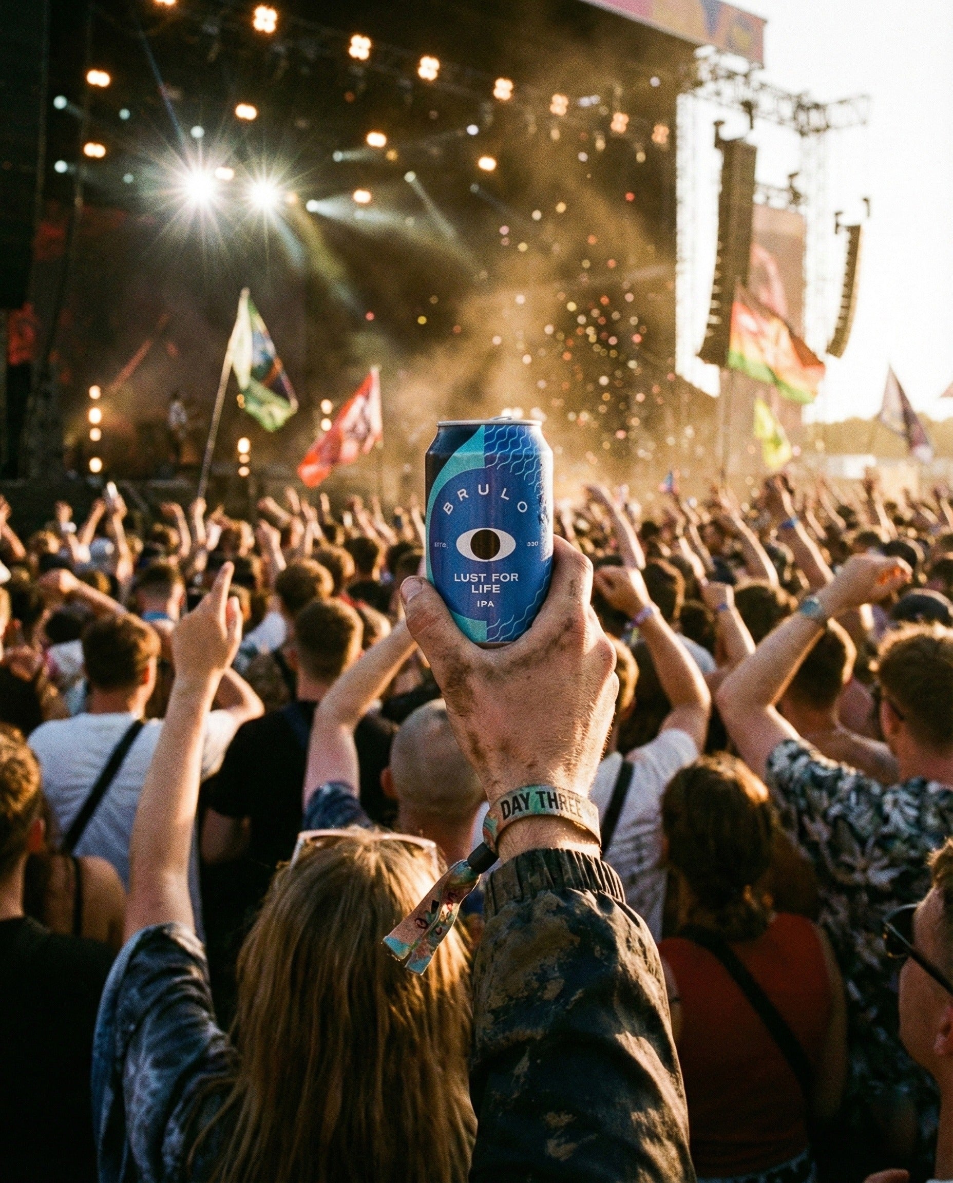 Brulo Lust for Life can held high above a festival crowd at golden hour, with a 'DAY THREE' wristband