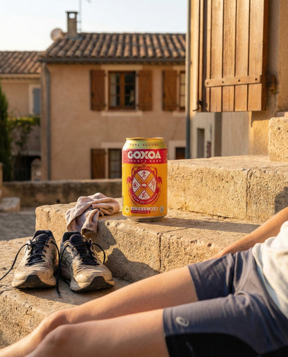 Goxoa Sportsbeer Blonde can on wooden bench by athletic track with Nike running shoes and towel at golden hour
