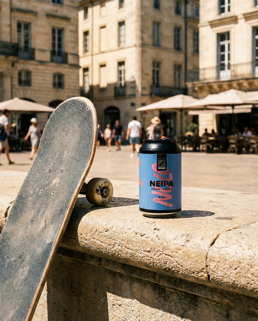 Prizm NOLO NEIPA can on a stone bench in a sun-baked southern French city plaza with a skateboard leaning beside it