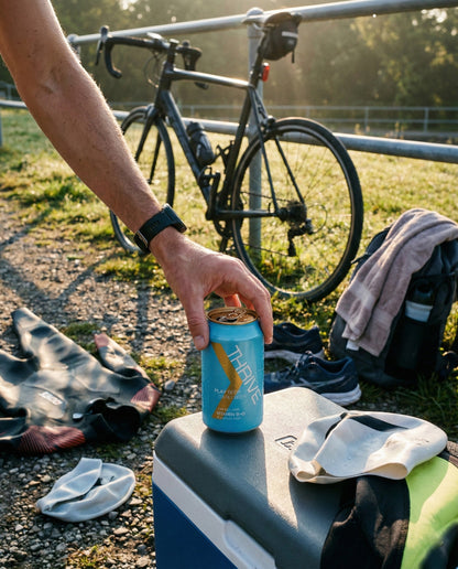 Thrive Play Beer can on cooler at triathlon transition with bike, wetsuit, swim caps and shoes at golden hour