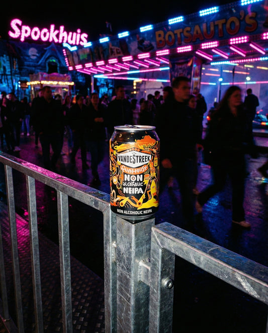 Vandestreek Funhouse can on a steel handrail at a Dutch night fairground with neon Spookhuis and bumper car signs